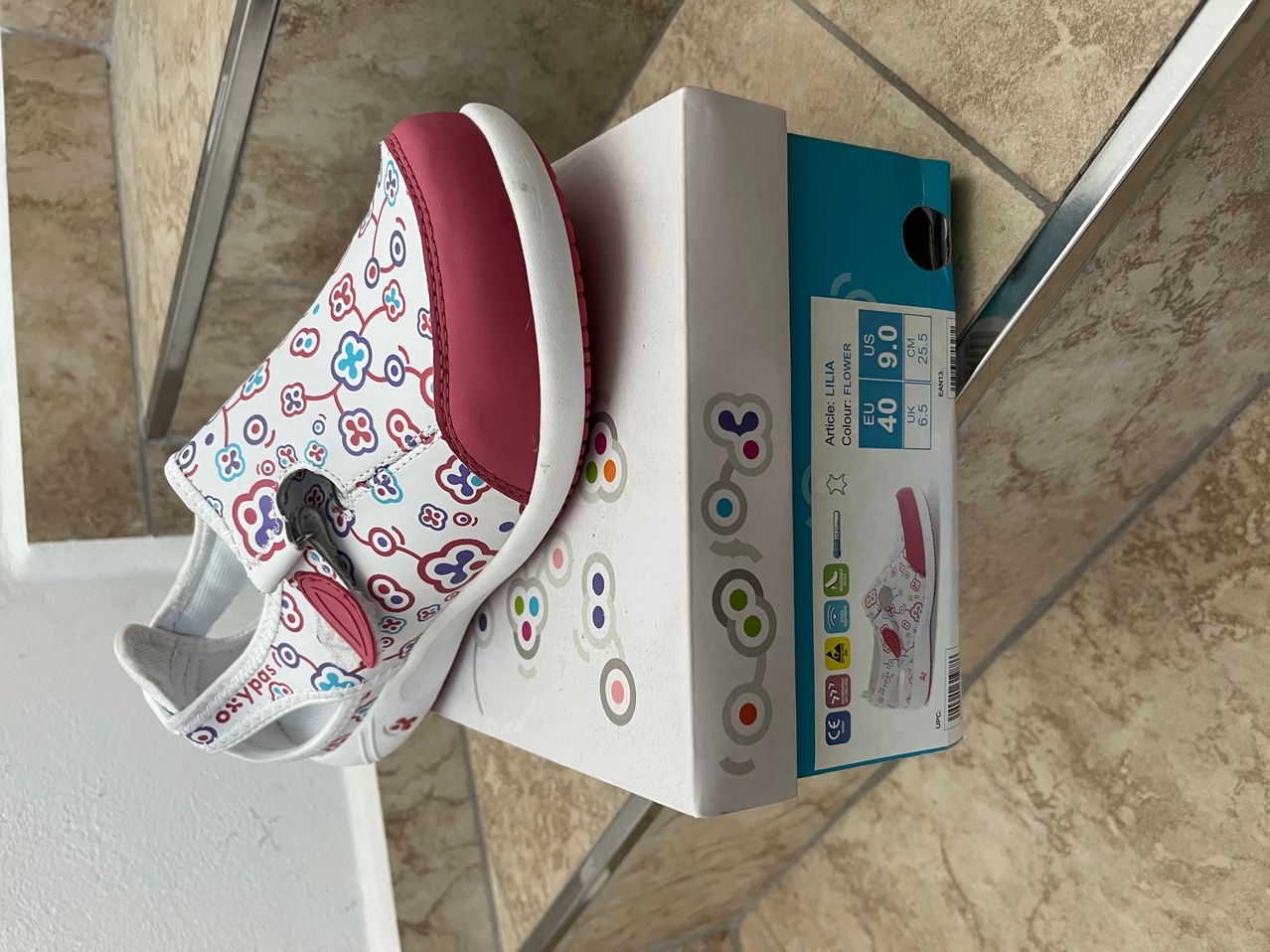 Ein Paar Kindersandalen mit Blumenmuster auf einer weißen Schachtel mit rotem Rand.