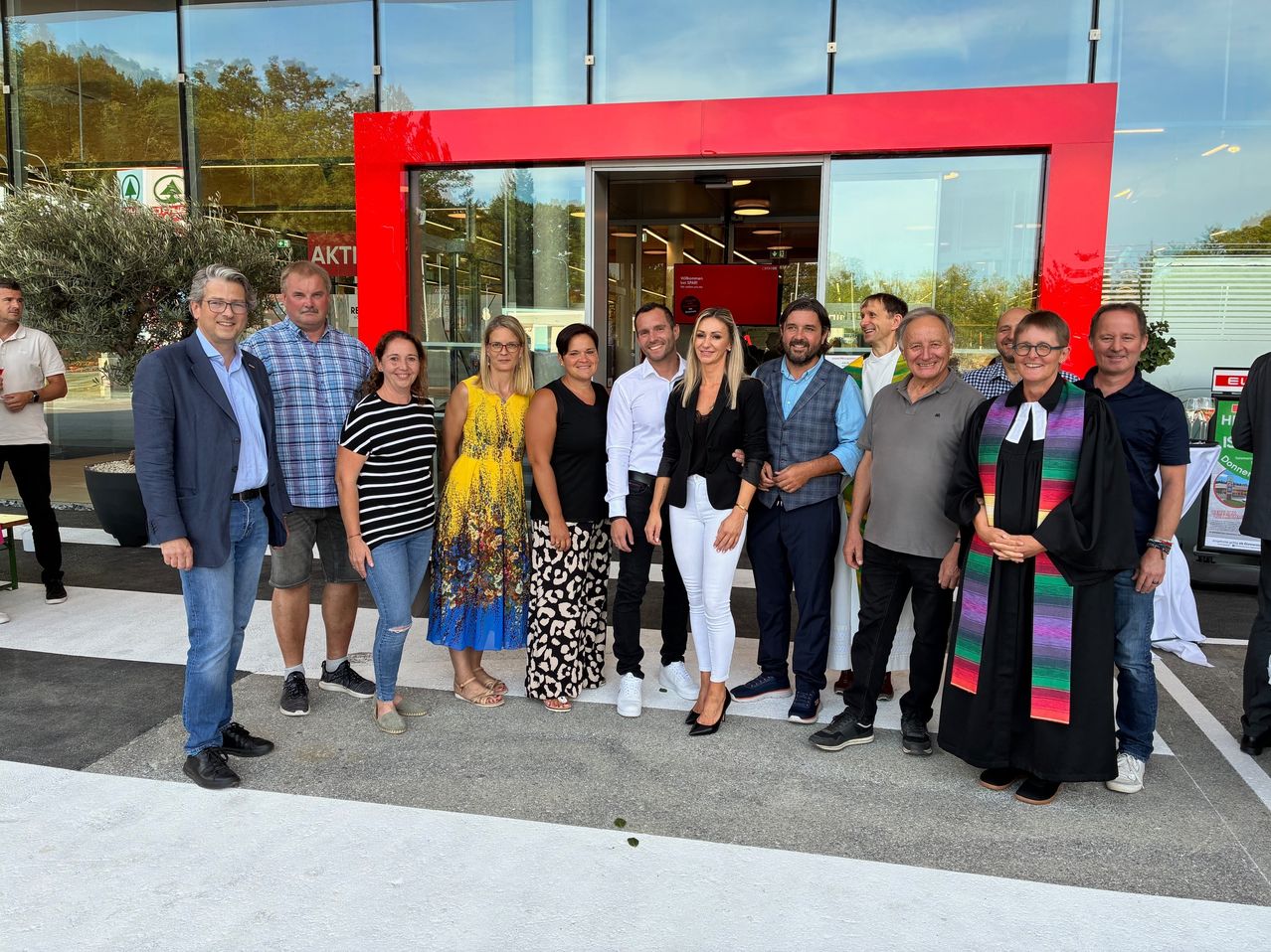 Eine Gruppe von Menschen in formeller Kleidung posiert für ein Foto vor einem roten Gebäude mit Glaswänden und -türen.