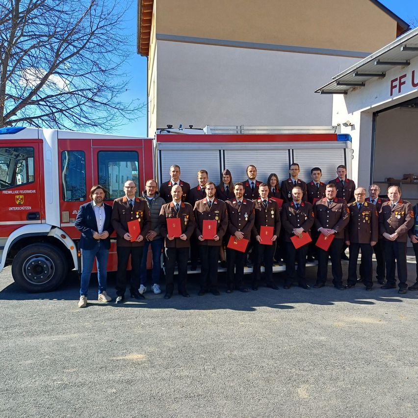 Eine Gruppe von Menschen in Uniformen steht vor einem Feuerwehrauto mit den Worten FF U am Gebäude.