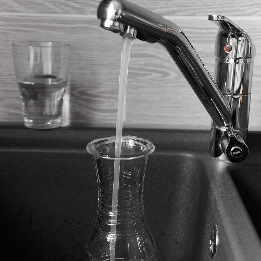 Ein Wasserhahn, aus dem Wasser in ein Glas und ein Becher auf einer Arbeitsplatte fließt.