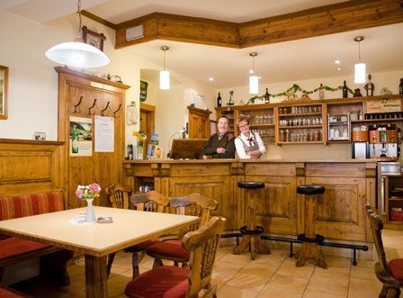 Ein Restaurant mit einer Holztheke, Stühlen und einem Holztisch mit einer Blumenvase. Zwei Personen stehen hinter der Theke.