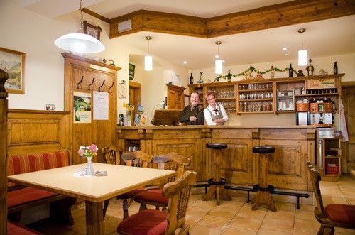 Ein Restaurant mit einer Holztheke, Stühlen und einem Holztisch mit einer Blumenvase. Zwei Personen stehen hinter der Theke.