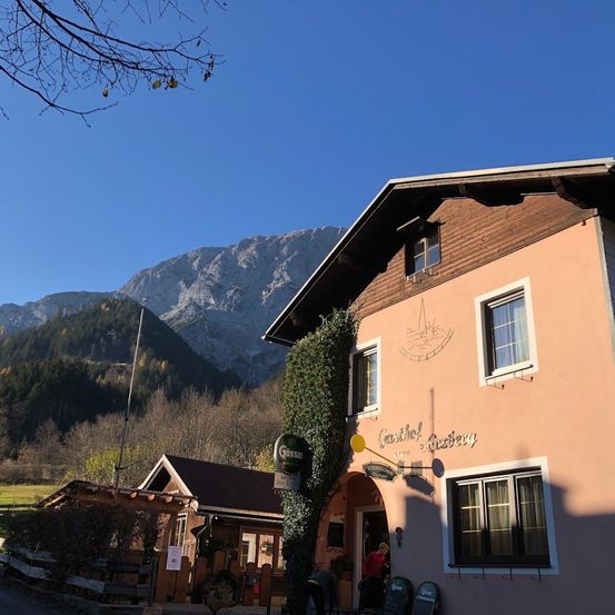 Ein Gebäude mit dem Schild 'Gasthof Gasthof' steht am Straßenrand mit einer Bergkette im Hintergrund.