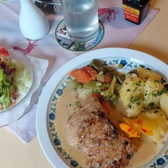 Ein Tisch zum Essen mit einem Teller Schweinekoteletts in cremiger Sauce, begleitet von Gemüse, und einem Glas Wasser.