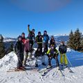 Eine Gruppe von Skifahrern und Snowboardern in Winterkleidung posiert auf einem verschneiten Berg, einige stehend und andere sitzend. Sie alle lächeln für die Kamera.