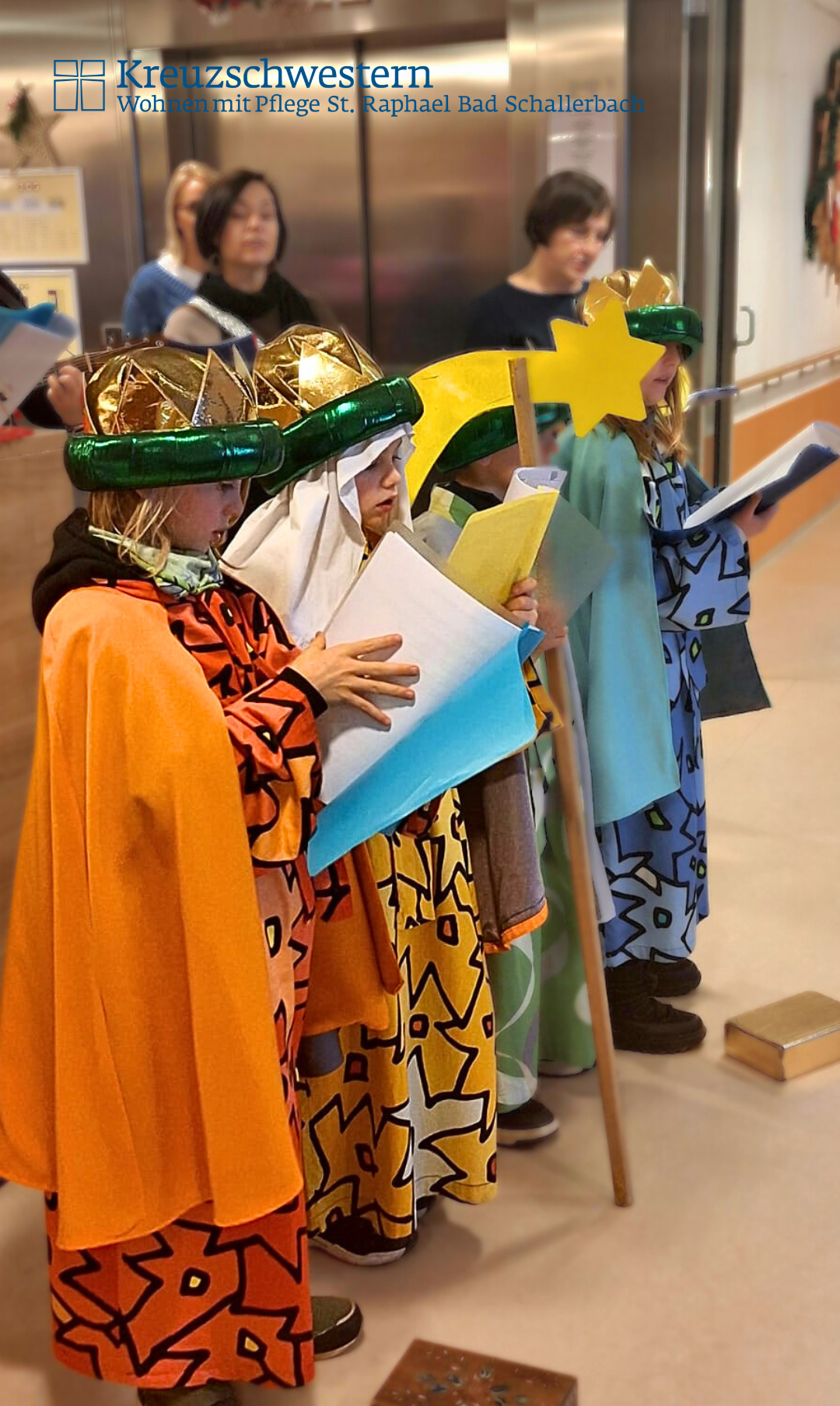 Eine Gruppe von Kindern, die als Weise Männer verkleidet sind, hält jeweils einen Papierstern und liest aus einem Buch.