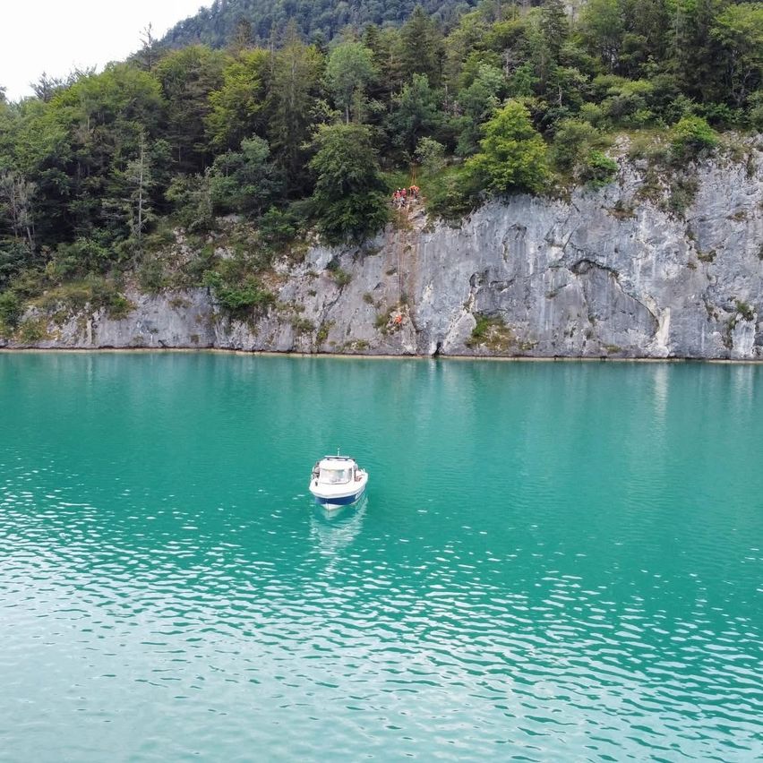 Ein kleines weißes Boot schwimmt in einem See mit einer felsigen Klippe auf einer Seite und Bäumen auf der anderen.