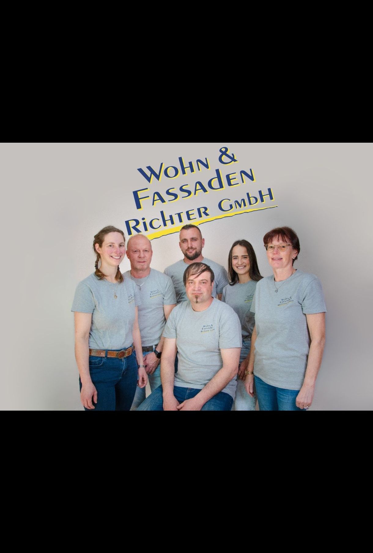 Eine Gruppe von fünf Personen in gleichen grauen T-Shirts posiert für ein Foto vor einem weißen Hintergrund mit dem Text 'Wohn & Fassaden Richter GmbH'.