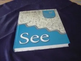 Ein blaues und weißes Buch mit dem Titel 'See' und einem Wellendesign auf dem Cover, auf einem dunkelblauen Tuch platziert.
