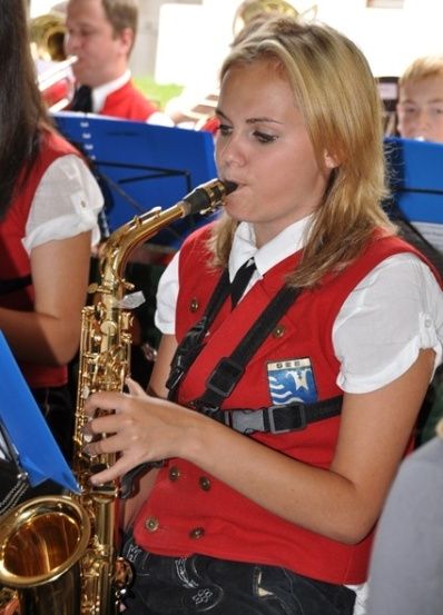 Eine Frau in einer roten Weste spielt Saxophon in einer Band mit anderen Mitgliedern hinter ihr.