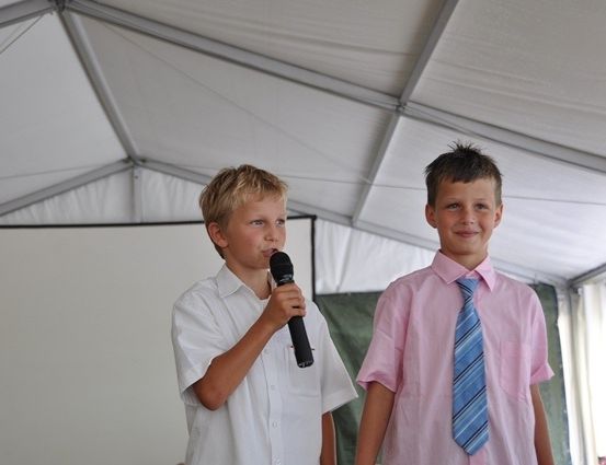 Zwei Jungen stehen unter einem weißen Zelt, einer hält ein Mikrofon und der andere lächelt in die Kamera.