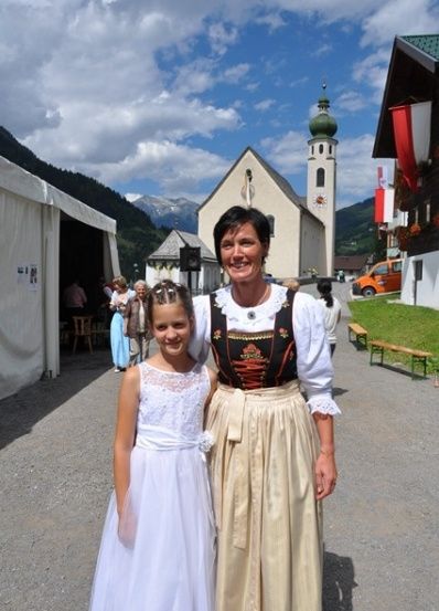Eine Frau und ein junges Mädchen stehen vor einer Kirche mit Bergen im Hintergrund.