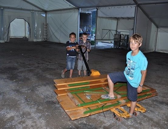 Drei Jungen stehen in einem großen Zelt mit einem Hubwagen. Die Jungen tragen Freizeitkleidung und scheinen für ein Foto zu posieren.