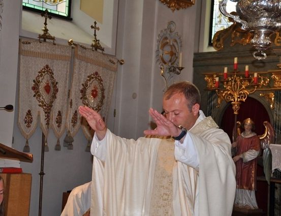 Ein Priester betet in einer Kirche mit einer Statue eines Engels hinter ihm.