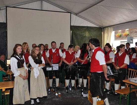 Eine Gruppe von Musikern in traditioneller Kleidung tritt in einem Zelt mit einer Projektionsleinwand und Publikum auf.