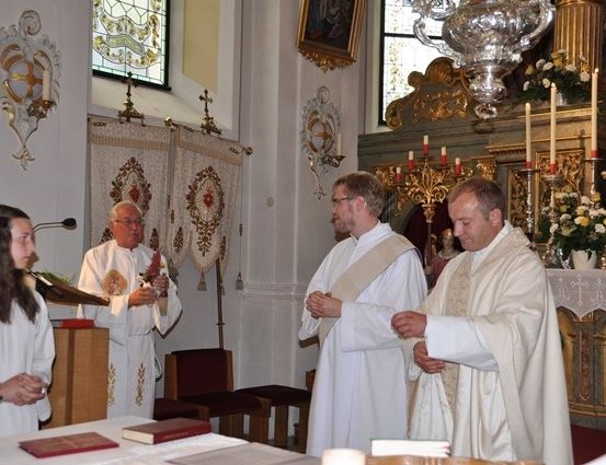 Drei Priester in weißen Gewändern stehen vor einem Altar in einer Kirche, mit Kerzen und einer Frau in der Nähe.