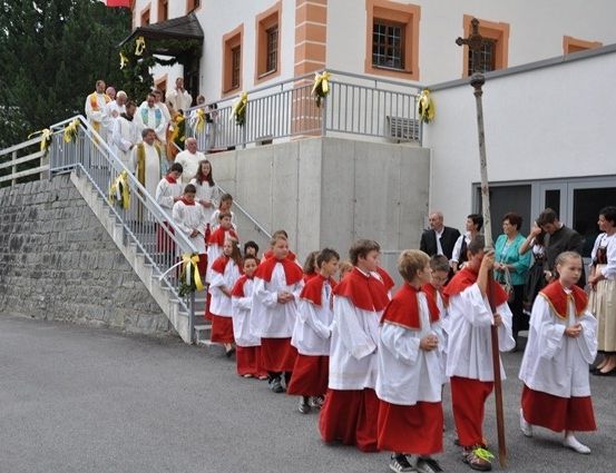Eine Gruppe von Kindern in roten und weißen Gewändern zieht in einer Prozession vor einer Kirche.