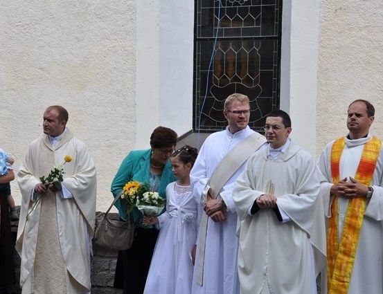 Eine Gruppe von Priestern und ein junges Mädchen in Weiß steht vor einem Kirchengebäude.