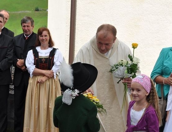 Ein Priester gibt einer kleinen Mädchen Blumen, während andere zusehen.