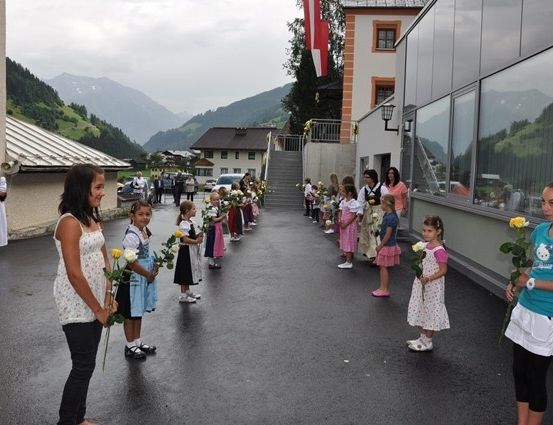 Eine Gruppe von Kindern mit Blumen steht in einer Reihe vor einem Gebäude mit Bergen im Hintergrund.