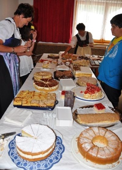 Ein langer Tisch voller verschiedener Desserts, einschließlich Kuchen und Gebäck, mit Menschen, die darum stehen.