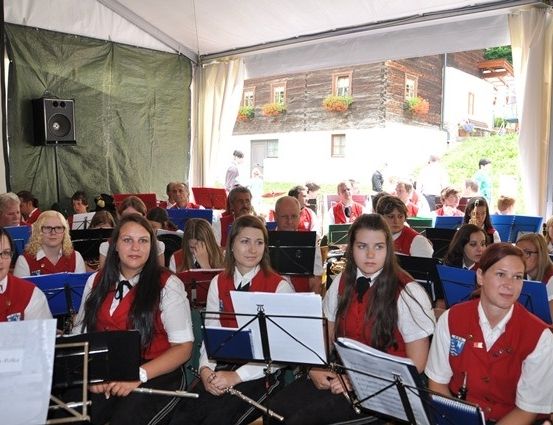 Eine Gruppe von Frauen in roten Westen und weißen Hemden sitzt auf Stühlen und spielt Musikinstrumente in einem Zelt.
