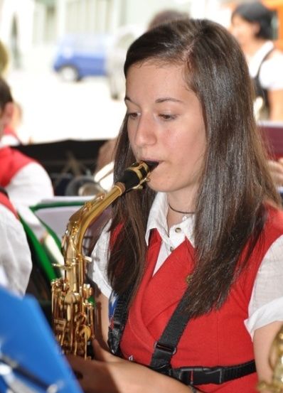 Eine junge Frau in einer roten Weste spielt während einer Bandprobe ein Saxophon.