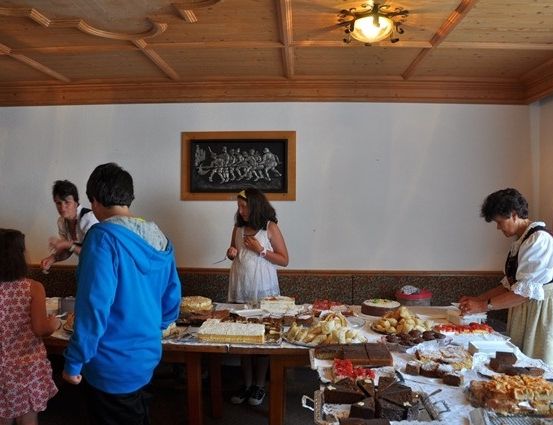 Eine Gruppe von Menschen versammelt sich um einen Tisch voller verschiedener Desserts in einem Raum mit Holzdecke und Wänden.
