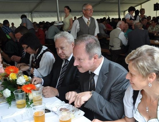 Eine Gruppe von Menschen in formeller Kleidung sitzt an einem Tisch mit Getränken und Essen, möglicherweise bei einer formellen Veranstaltung.