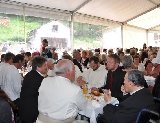 Eine große Gruppe von Menschen in formeller Kleidung sitzt an Tischen in einem Zelt und genießt eine Mahlzeit und Getränke. Einige tragen weiße Gewänder.