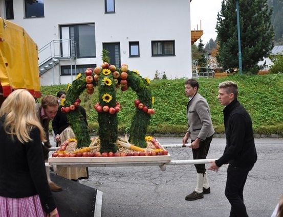 Eine Gruppe von Menschen trägt eine große Blumenarrangement auf einem Anhänger in einer Straße. Das Arrangement besteht aus Früchten und Blumen.