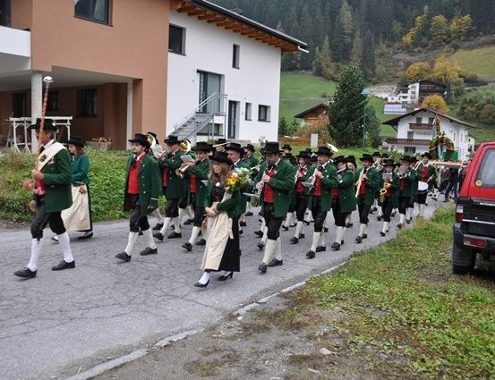 Eine Blaskapelle in grünen Uniformen und schwarzen Hüten spielt Instrumente, während sie eine Straße entlang gehen.