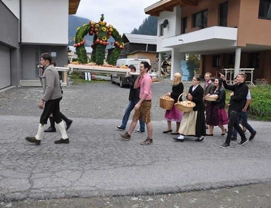 Eine Gruppe von Menschen geht mit Körben voller Früchte auf einer Straße, mit einer großen Apfeldekoration im Hintergrund.