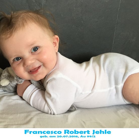 Ein lächelndes Baby namens Francesco Robert Jehle, geboren am 20.07.2016, liegt auf einem Bett mit einem Kuscheltier.