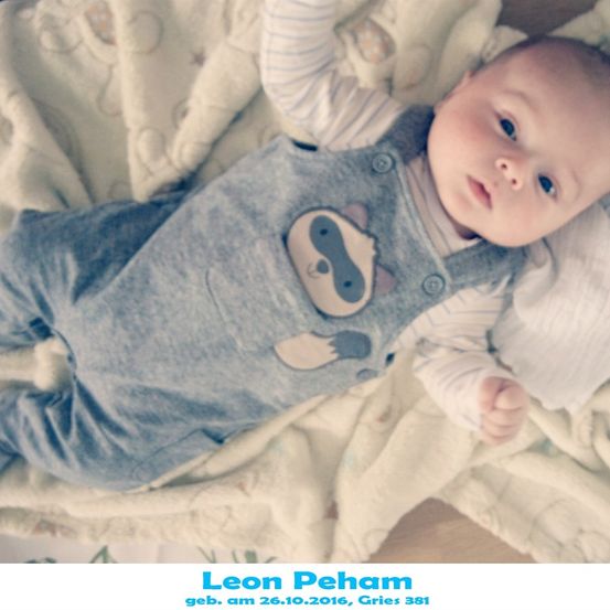 Ein Babyjunge namens Leon Peham, geboren am 26. Oktober 2016, liegt auf einer Decke, trägt einen blauen Overall mit Faultier-Design und schaut direkt in die Kamera.