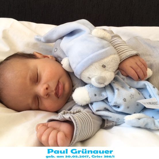 Ein Babyjunge schläft friedlich auf einem Bett und hält ein weißes Kuscheltier. Er trägt eine blaue Mütze und passende blaue Schlafanzug. Das Bild ist vom 30. Mai 2017.