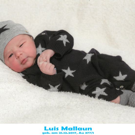 Ein neugeborener Junge, Luis Mallaun, geboren am 21.12.2017, liegt auf einer weißen Decke und trägt ein schwarzes Outfit mit Sternenmustern.