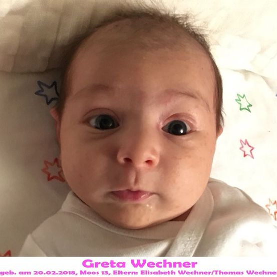 Ein Babymädchen mit kahlem Kopf und großen Augen liegt auf einer weißen Decke mit bunten Sternen. Das Babymädchen heißt Greta Vechner, geboren am 20. Februar 2018.