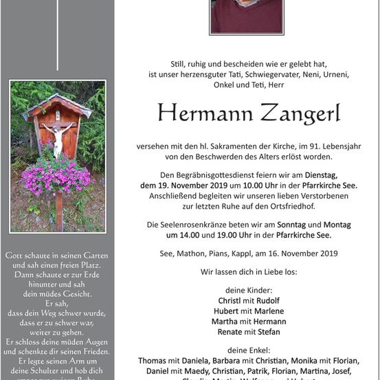 Ein Gedenkposter für Hermann Zangerl, mit einem kleinen hölzernen Kruzifix und Blumen, mit Text auf Deutsch über sein Leben und seinen Tod.