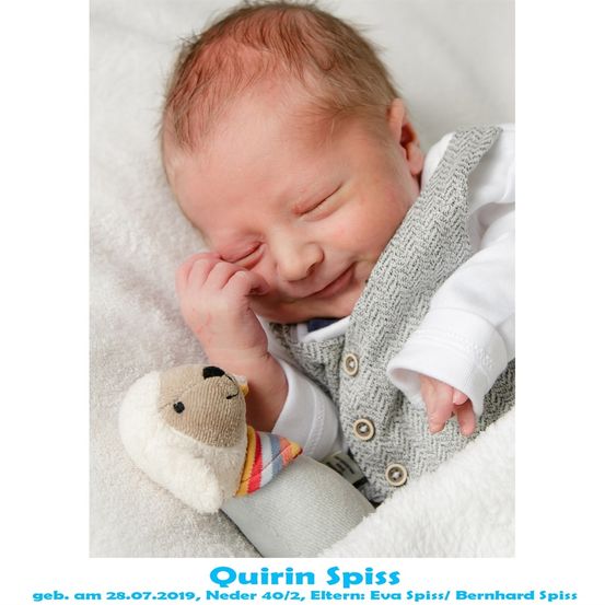 Ein neugeborener Junge, Quirin Spiss, geboren am 28.07.2019, schläft friedlich auf einer weißen Decke und hält ein Kuscheltier. Er trägt eine graue Weste und ein weißes Langarmshirt.