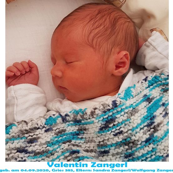 Ein neugeborener Junge, Valentin Zangerl, geboren am 4. September 2020, schläft friedlich auf einem Bett mit einer blau-weiß gestrickten Decke.