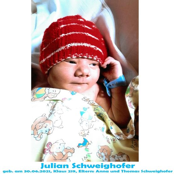 Ein Neugeborenes namens Julian Schweighof, geboren am 30.06.2021, trägt eine rote gestreifte Mütze und ein blaues Armband, liegt auf einem Bett mit einer weißen Decke.