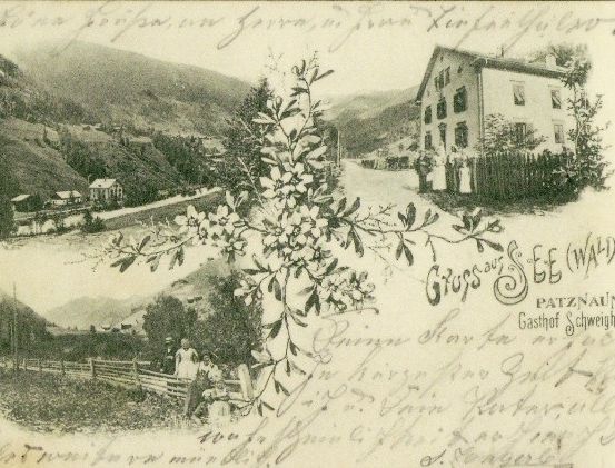 Ein altes Postkartenbild zeigt eine Berglandschaft mit einem Haus, einer Straße und Menschen, die an einem Zaun stehen. Das Bild hat handgeschriebenen Text und einen Wasserzeichen.