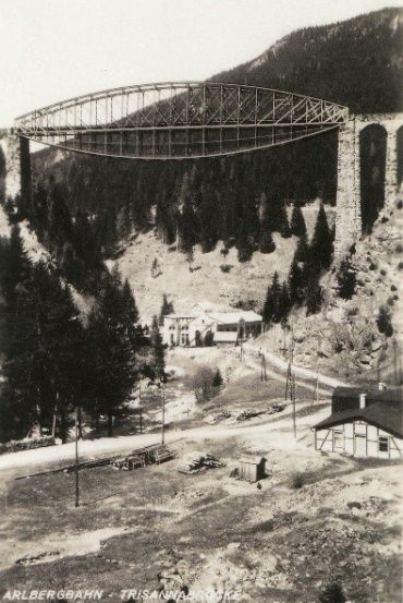 Ein Schwarz-Weiß-Foto einer Brücke über einem Tal mit einem Haus und Bäumen im Hintergrund.