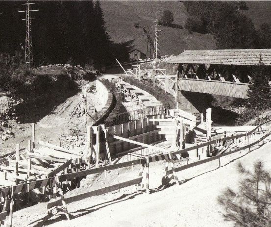 Schwarz-Weiß-Bild einer Baustelle mit Arbeitern, die eine Brücke über eine Straße bauen.