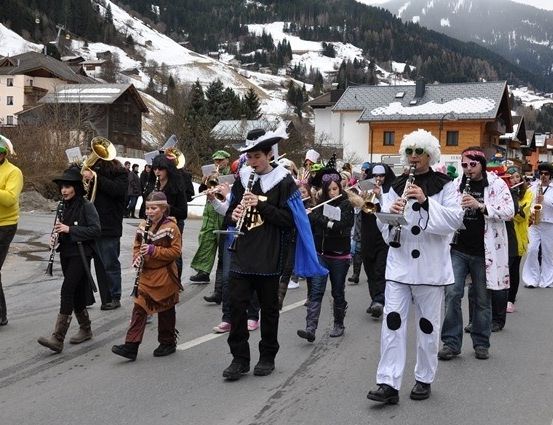 Eine Gruppe von Menschen in verschiedenen Kostümen zieht auf einer verschneiten Straße durch eine Parade. Einige spielen Musikinstrumente.