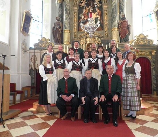 Eine Gruppe von Menschen in traditioneller Kleidung posiert für ein Foto in einer Kirche. Sie sitzen und stehen vor einem Altar.