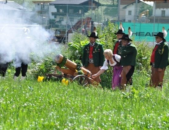 Eine Gruppe von Menschen in traditioneller Kleidung feuert eine Kanone auf einem Feld ab.