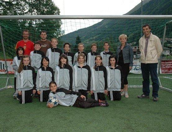 Eine Gruppe junger Fußballspieler in passenden Uniformen posiert für ein Foto vor einem Fußballtor mit einem Gebirgshintergrund.