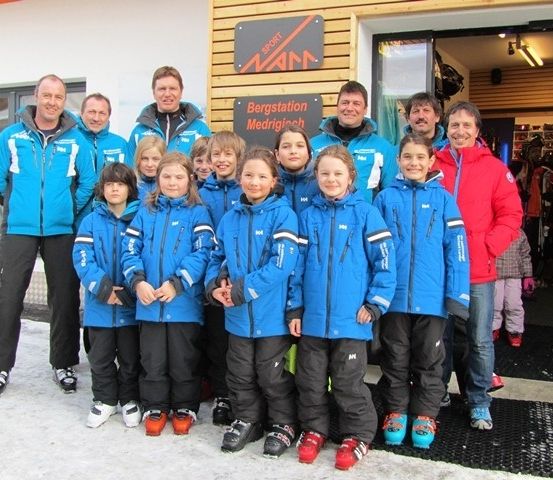 Eine Gruppe von Menschen in blauen und roten Skijacken posiert für ein Foto vor einem Gebäude.